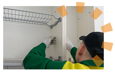 A handyman works on taking out a screw connecting adjoining upper kitchen cabinets.