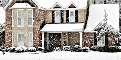 Image of a two-story house covered in snow during a light snow fall.