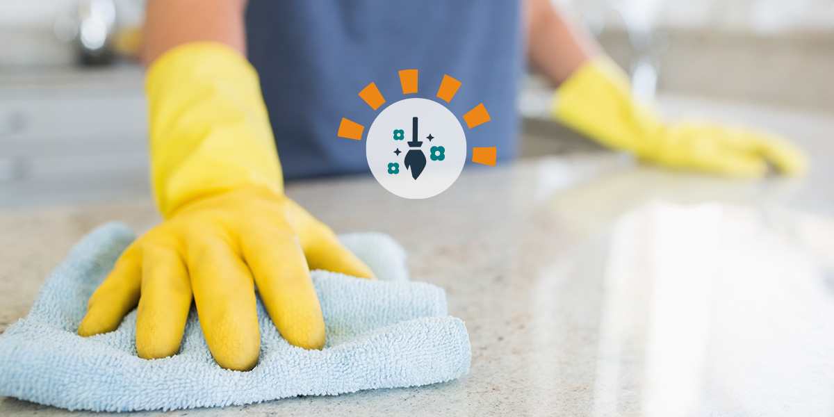 A woman with yellow gloves cleaning a countertop.