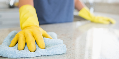 A woman with yellow gloves cleaning a countertop. 