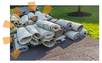 Stacks of old carpet rolled up on driveway for removal.