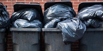 Row of Black Garbage Cans Overflowing With Trash Bags
