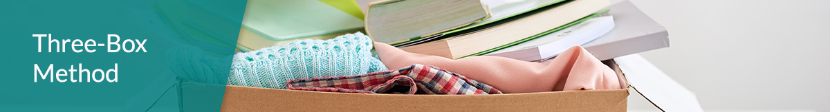 Man holding a book to put in a cardboard box full of items.