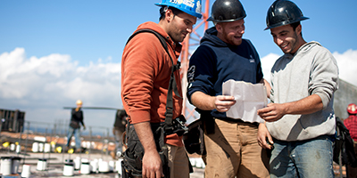 Three construction workers in hard hats at a jobsite and looking at construction plans.