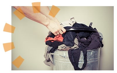 A metal trash can filled with old unwearable clothing.