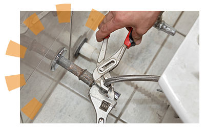 A person disconnecting a water line from a toilet with a pair of wrenches.