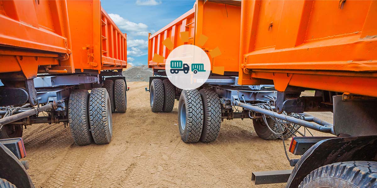 Four orange dump trailers lined up in the dirt.