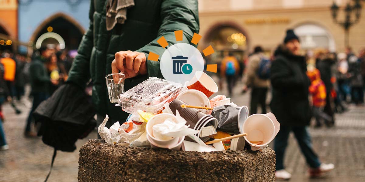 A person puts a cup into an overflowing stone trash bin.