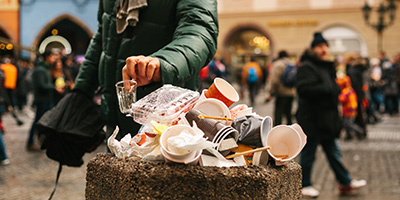 A person puts a cup into an overflowing stone trash bin.