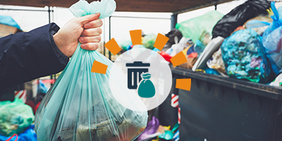 A hand holding a green trash bag in front of several overflowing trash bins.