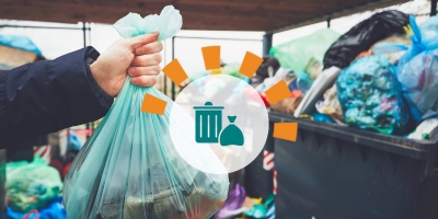 A hand holding a green trash bag in front of several overflowing trash bins.
