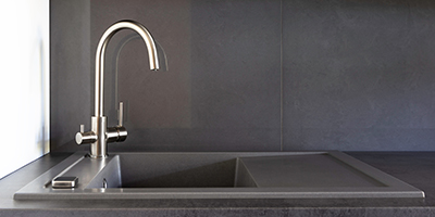 A brushed nickel kitchen faucet with black countertops.