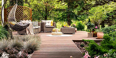 Updated backyard with wooden terrace, garden with potted flowers and wicker swing chair. 