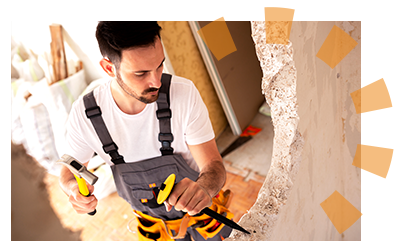 A man tears down a plaster wall with a hammer and chisel.