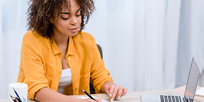 Woman smiling at a desk with a laptop, notebook and calculator as she deducts home project expenses from her tax return.