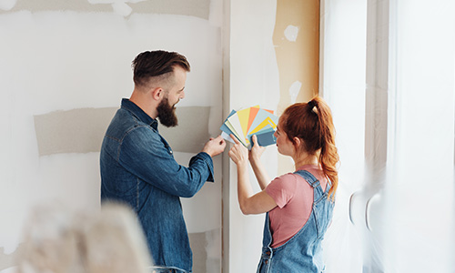 A couple selecting a paint color from paint samples in front of an unfinished wall. 