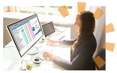 A young woman in an office working on a spreadsheet on a desk monitor.