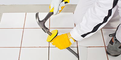 Diyer with gloves hammering chisel to remove ceramic tile.