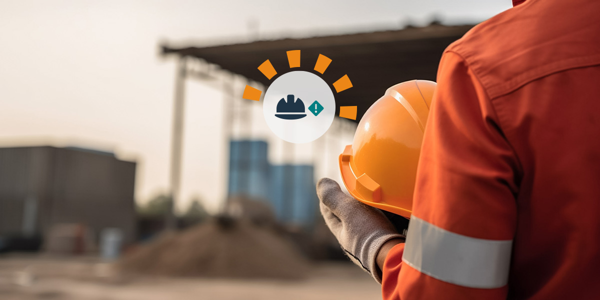 Construction worker wearing protective, reflective equipment holding an orange hard hat at a jobsite.