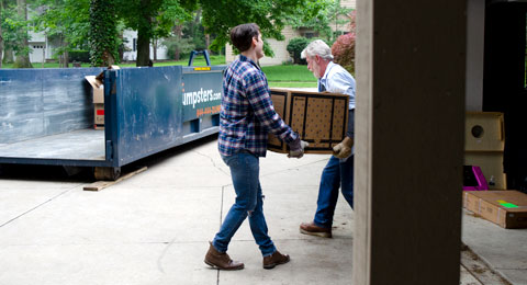 Two Men Loading a Roll Off Dumpster With Household Junk.