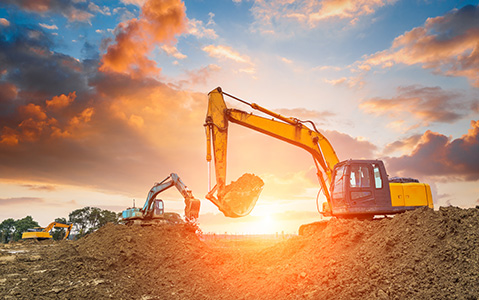 Two yellow excavators with backhoes moving earth on a jobsite at dawn.