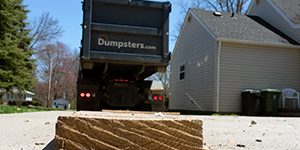 dumpster truck preparing to roll off dumpster onto wooden planks