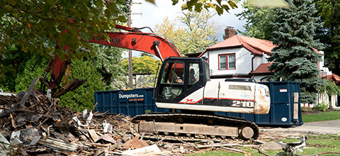 A demolition backhoe moving and surrounded by debris.