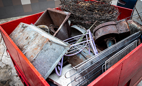 A red dumpster filled with used metal wiring, containers, grates and rods. 