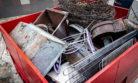 A red dumpster filled with used metal wiring, containers, grates and rods.