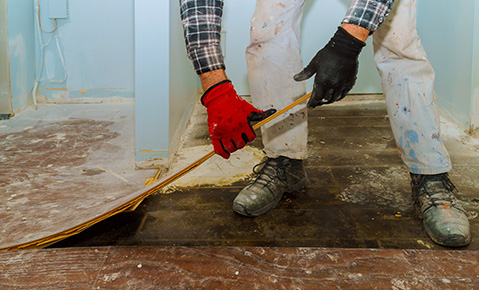 A worker pulling up linoleum flooring.