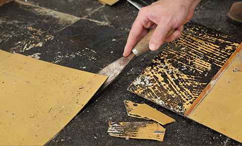 A person peeling off laminate tiles from a floor.