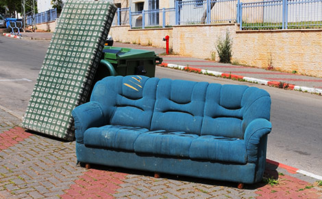 An old blue couch and other trash on the curb. 