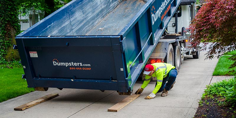 Driver Laying Down Wood Under Roll Off Dumpster.