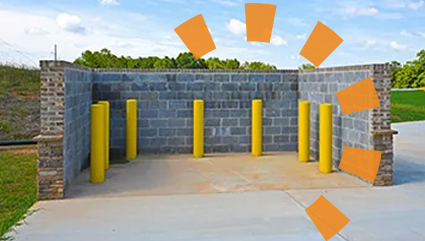 Cinderblock commercial dumpster enclosure with yellow guard posts spaced apart.