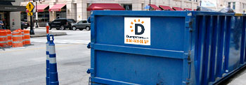 A Blue Roll Off Dumpster on an Urban Street Near Traffic Cones.