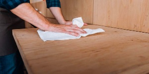 Man cleaning wood table with cloth.