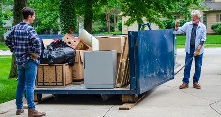 Father and son looking at a roll off dumpster filled with bulk waste in the driveway.