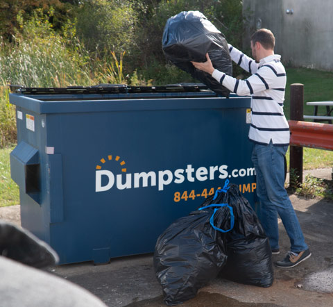 Man Filling Front Load Bin With Filled Trash Bags