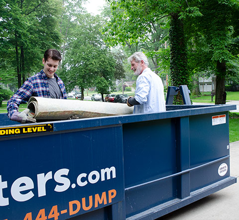 Two Men Filling Small Roll Off Dumpster With Junk