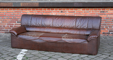 Brown leather couch in front of brick wall.