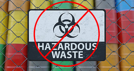 No Hazardous Waste sign hanging on a chain link fence in front of hazardous waste barrels.