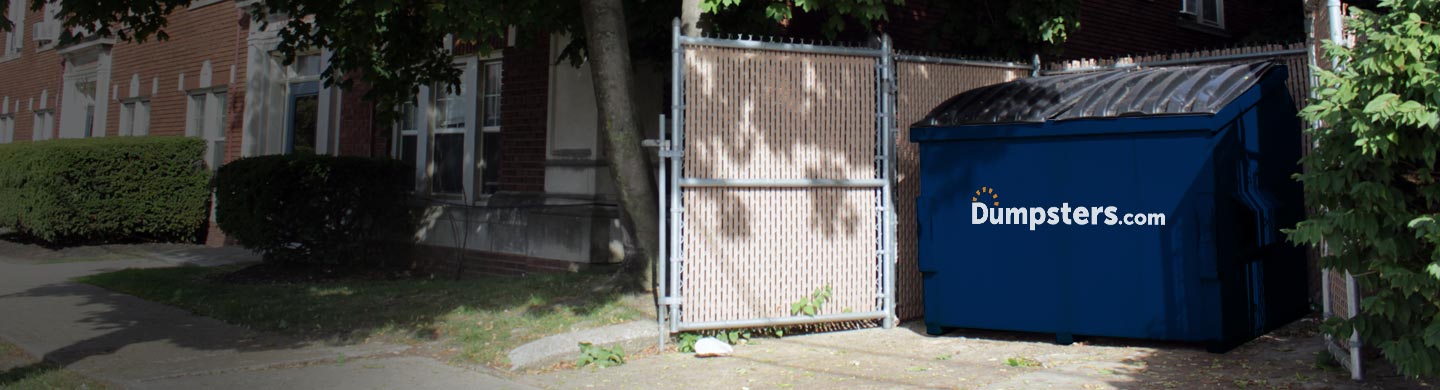 commercial dumpster in an enclosure beside an apartment building