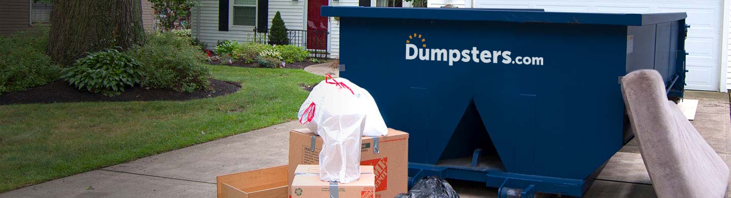 cardboard boxes and garbage bags piled next to a dumpster