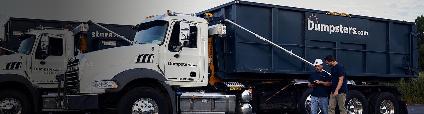 two dumpsters.com drivers check a tablet in front of their trucks