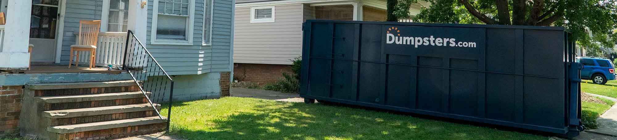 Dumpsters.com Roll Off Dumpster in Residential Driveway With Blue House.