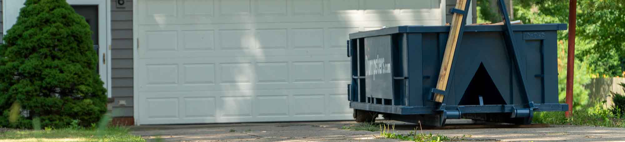 Roll Off Dumpster in Residential Driveway Next to Blue House.