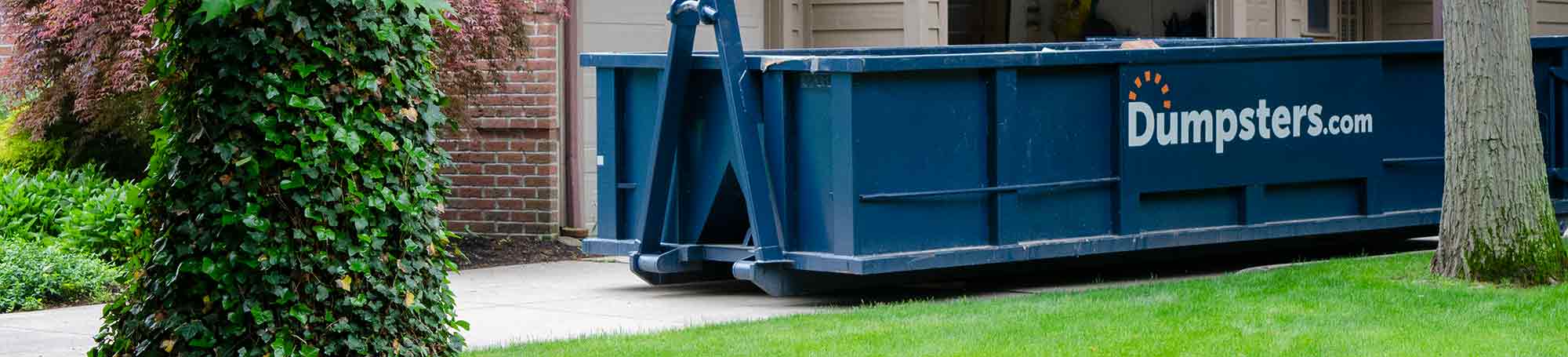 A Blue Roll Off Dumpster in the Driveway Outside of a Garage.