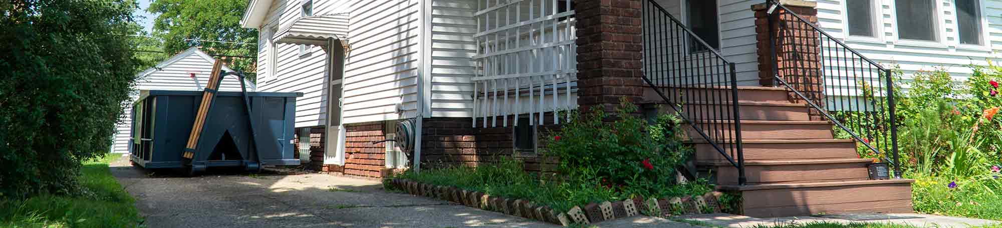 Roll Off Dumpster in a Residential Driveway Next to White and Brick House.