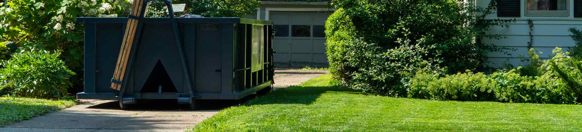 Roll Off Dumpster in Residential Driveway Next to Blue House.