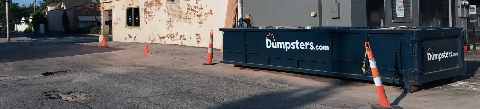 Roll Off Dumpster in Urban Parking Lot Near Orange Traffic Cones.